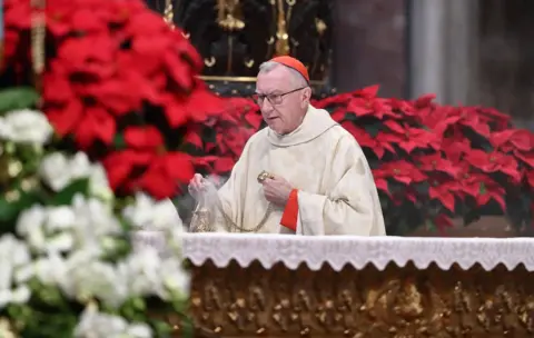 Getty Images Cardinal Pietro Parolin wears a red cap on his head while he holds a smoking urn on a table against a backdrop of red chrysantheums during the Holy Mass on the occasion of the Solemnity of Mary, Mother of God, in St. Peters Basilica, Vatican City on 1 January.