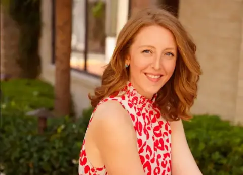 Levels A red-haired woman in a red and white dress smiling and pictured outside